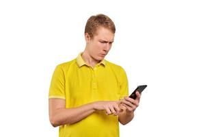 Puzzled young man with smartphone tapping touchscreen, man in T-short isolated on white background photo