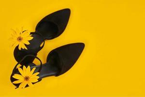 Suede black court shoes with yellow Topinambur flower bud on strap, yellow background, trendy shoes photo