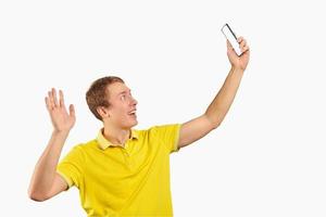 Funny guy in bright yellow T-shirt video chatting using video call with phone, smiling young man photo