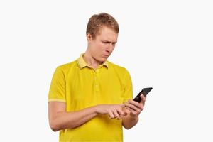 Puzzled young man with smartphone tapping touchscreen, man in T-short isolated on white background photo