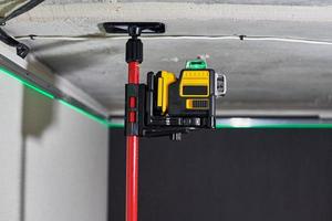 Laser level measuring tool with visible green laser beam on wall of unfinished apartment photo