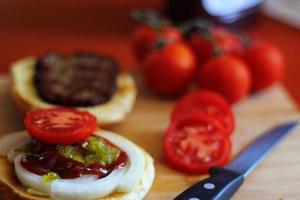 The hamburger is being prepared and served with sliced tomatoes, onions, pickles. on a wooden cutting board in the kitchen photo