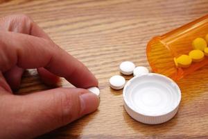 A man's hand is taking pills from an orange pill bottle on a wooden table, medicine pill on wooden table. photo