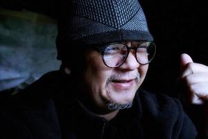 hombre asiático barbudo con chaqueta negra y gorro de punto. trabajando en una habitación oscura y sonriendo felizmente foto