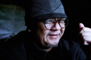 Bearded Asian man in black jacket and knitted hat. Working in a dark room and smiling happily photo