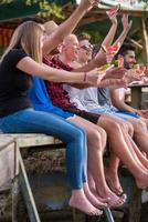 friends enjoying watermelon while sitting on the wooden bridge photo