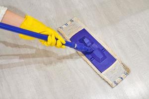 Girl in protective gloves cleaning floor using flat wet mop. photo