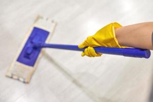 Girl in protective gloves cleaning floor using flat wet mop. photo