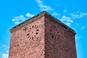 Old abandoned red brick tower with round clock on facade, vintage masonry, blue sky background photo