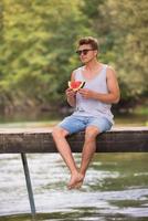 hombre disfrutando de la sandía mientras está sentado en el puente de madera foto