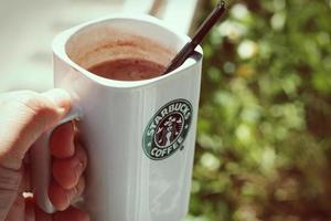 taza de café starbucks colocada sobre rocas alrededor de una fogata de camping con fondo borroso, tonos modernos. foto