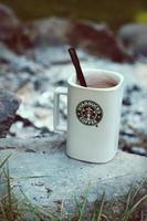 Starbucks Coffee Mug Placed on rocks around a camping campfire with blurred background, modern tones. photo