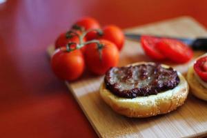 The hamburger is being prepared and served with sliced tomatoes, onions, pickles. on a wooden cutting board in the kitchen photo