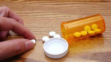 A man's hand is taking pills from an orange pill bottle on a wooden table, medicine pill on wooden table. photo