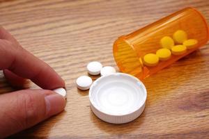 A man's hand is taking pills from an orange pill bottle on a wooden table, medicine pill on wooden table. photo