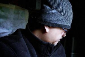 Bearded Asian man in black jacket and knitted hat. Working in a dark room and heading down to work photo