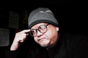 Bearded Asian man in black jacket and knitted hat. Working in a dark room and thinking to work photo