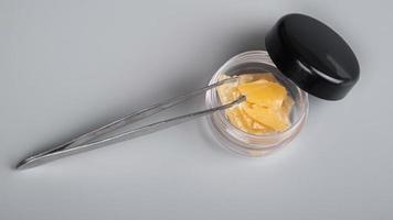 high thc cannabis concentrate,tweezers and container with piece wax extract on gray background photo