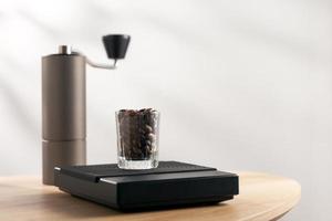 Dark roasted coffee beans in a clear glass on a digital scale and a Manual coffee grinder photo