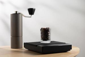 Dark roasted coffee beans in a clear glass on a digital scale and a manual coffee grinder photo