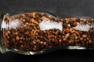 A mixture of seasonings, spices and herbs in a glass mill on a black background. photo