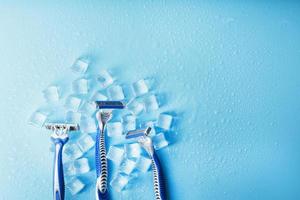 tres máquinas de afeitar sobre un fondo azul helado con hielo. el concepto de limpieza y frescura helada foto