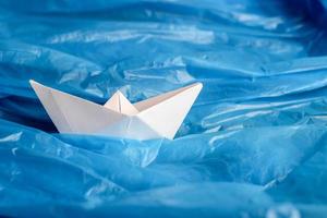 nave origami de papel blanco entre una bolsa de plástico azul como si estuviera en olas de agua. foto conceptual