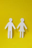 Silhouettes of a man and a woman are carved from white paper, standing side by side on a yellow background. The concept of love, relationships, family. Vertical photo