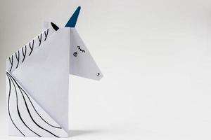 White unicorn made in the origami technique on the left side of the photo on a white background. With place for your text.