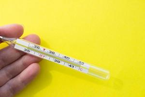 Mercury thermometer in hand on yellow background. Close up photo. Thermometer shows a temperature of 38.7 degrees Celsius photo