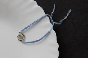 pulsera trenzada hecha a mano azul claro con chakra vishuddha en el borde de un plato blanco como la nieve foto
