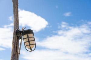 farola retro, bombilla colgada en un poste eléctrico de madera. pilar vintage con lámpara. claro fondo de cielo azul vacío, espacio de copia. linterna vieja foto