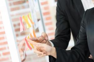 pointing on glass wall with glued colorful paper notes. Note paper reminder schedule board. Business people meeting and use post it notes to share idea. Discussing - business, teamwork, concept photo