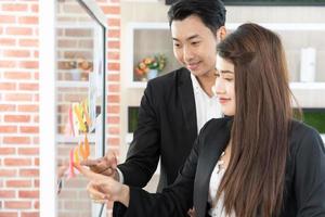 businesspeople office worker reading sticky notes on planning glass board. Business team pointing on keywords in sticky notes and business report to brainstorming about planning strategy of business. photo