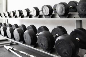 pararse con pesas. Sala de deportes y fitness. equipo de entrenamiento con pesas. juego de mancuernas negras, muchas mancuernas en el rack en el gimnasio deportivo foto