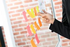 pointing on glass wall with glued colorful paper notes. Note paper reminder schedule board. Business people meeting and use post it notes to share idea. Discussing - business, teamwork, concept photo