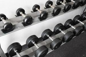 pararse con pesas. Sala de deportes y fitness. equipo de entrenamiento con pesas. juego de mancuernas negras, muchas mancuernas en el rack en el gimnasio deportivo foto