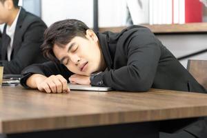 hombre de negocios asiático usa traje formal sentado en la oficina sintiéndose aburrido y dolor corporal por el síndrome de la oficina foto