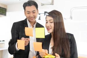 businesspeople office worker reading sticky notes on planning glass board. Business team pointing on keywords in sticky notes and business report to brainstorming about planning strategy of business. photo