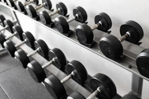 pararse con pesas. Sala de deportes y fitness. equipo de entrenamiento con pesas. juego de mancuernas negras, muchas mancuernas en el rack en el gimnasio deportivo foto