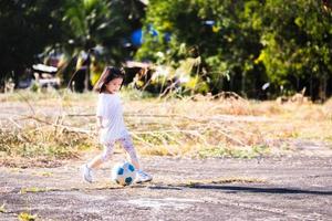 imagen de retrato niña activa de 5 años. niño jugando al fútbol en verano. niño feliz corriendo con gracioso. los niños hacen ejercicio en el campo de cemento. espacio vacío para ingresar texto. bebé asiático practicando. foto