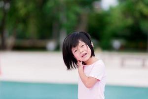 Asian child is scratching his neck due to itching. Hot weather in the summer time. Cute girl is sweating on the face. Kid aged 4 years old wearing soft pink dress. photo