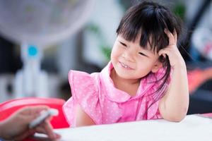 Adorable kid girl sweet smile in the small classroom at home school. Child thinking about concept her artwork with teacher. Children wearing pink shirt and polka dots pattern. Lady 4 years old. photo