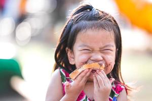 Portrait image of child 4-5 years old. Happy Asian girl eating Chocolate Bread. Children enjoy eating sweets. World Chocolate Day. Sweet smile. Kid mouth stained with sweets. Empty space. photo