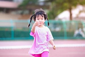 Cute 4 year old Asian girl running and having fun. Happy child was wearing a pink dress. Children braided two braids. Sweet smile kid. photo
