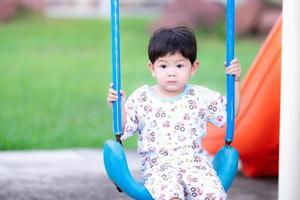 Children sit on the swing. Child shows a calm expression. Boy play toys machine in the playground on a hot summer or spring evening. Baby aged is 2 years old.
