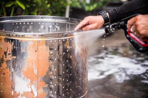 Man's hands of contractor washes dirt of drum by removing machine and washing it like experienced person. He grasps stainless steel bucket and holds high pressure hydration hose to remove the dirt. photo