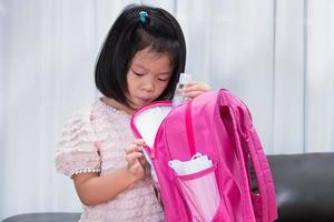 Portrait image child 5 years old. Kindergarten students are packing bags to prepare for school. Asian girls checked the equipment and the notebooks. Kid with a pink backpack. Back to school photo