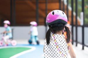 Rear back view. Children playing mini bike on playground street. Child are learning traffic signs and driving on road. Kid wearing pink helmet. Fun learn concept through play for good memory. photo