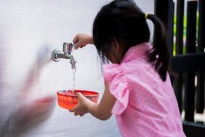 Selective focus. Child fill a bowl with water for making watercolor art, handicrafts. On the back of a 4 year old girl wearing a pink shirt. photo